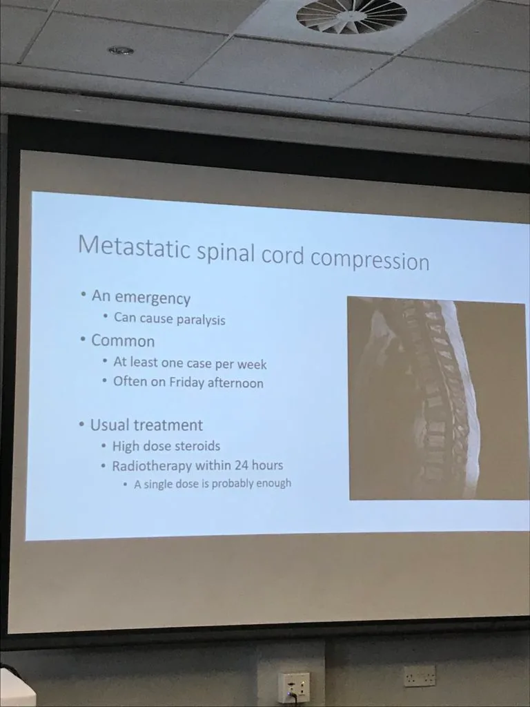 A conference slide on metastatic spinal cord compression, beside a spinal scan: an emergency that can cause paralysis, common, usually treated with high dose steroids and radiotherapy within 24 hours.
