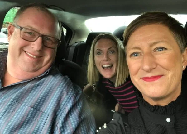 Three friends squeezed together for a selfie in a car.