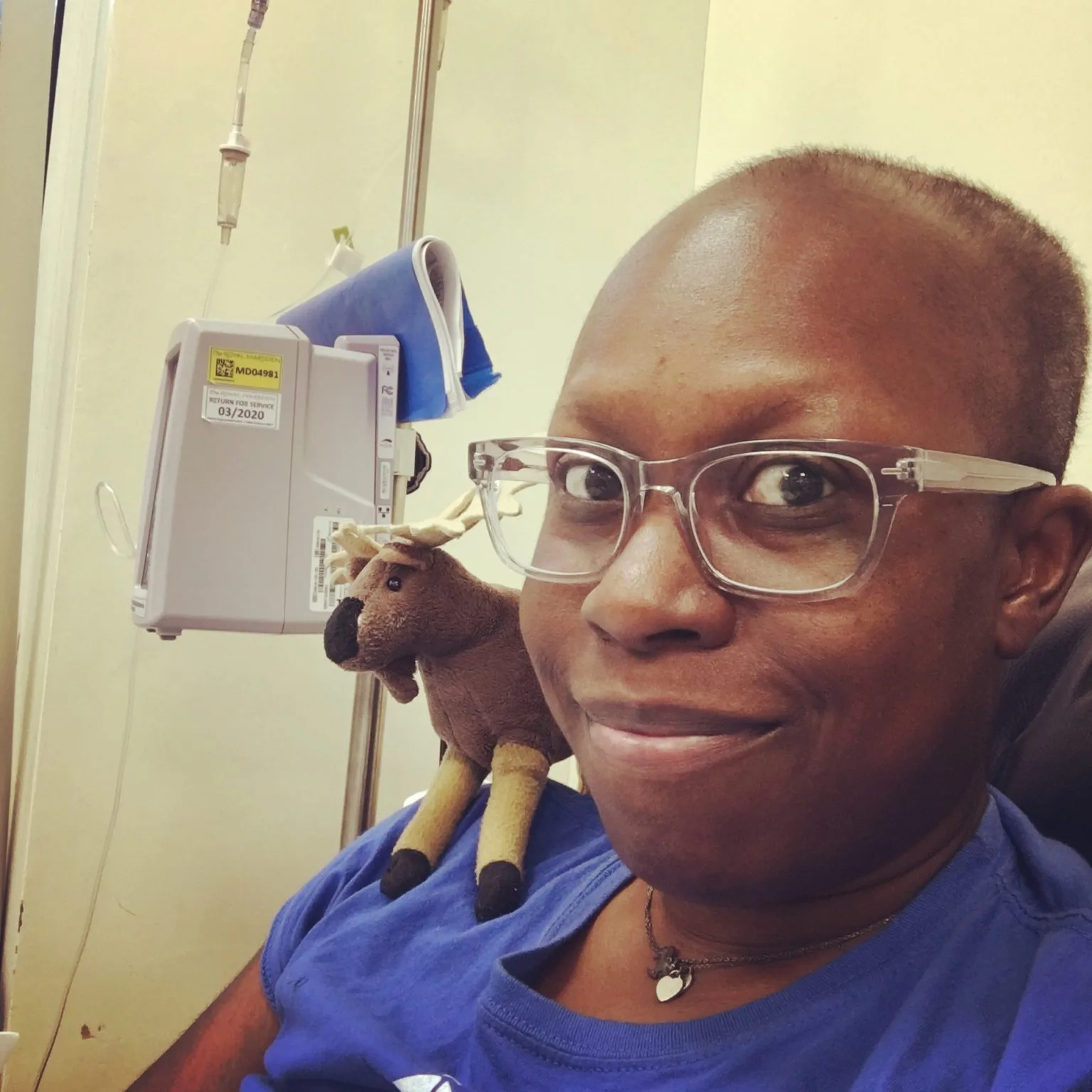 Miranda Ashitey in a hospital chair during treatment, a drip beside her and a small toy moose on her shoulder.