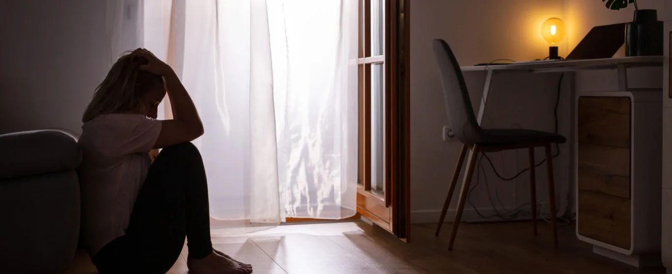 Side view full length shot of a sad depressed woman sitting on the floor and crying at home