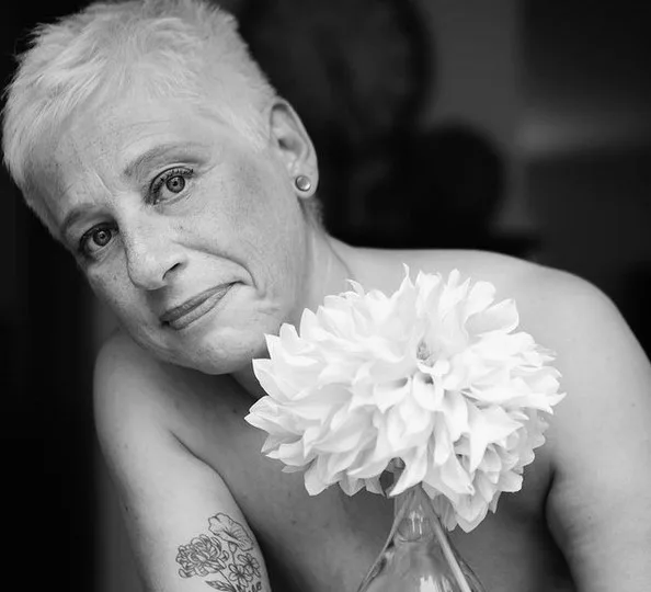 A black and white portrait: a woman with cropped hair holding a white chrysanthemum against her chest.