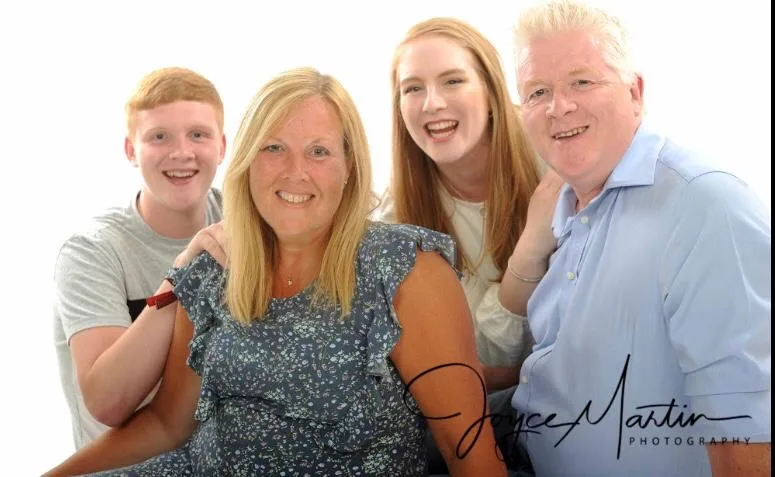 A family of four, two parents and two teenagers, arm in arm for a portrait.