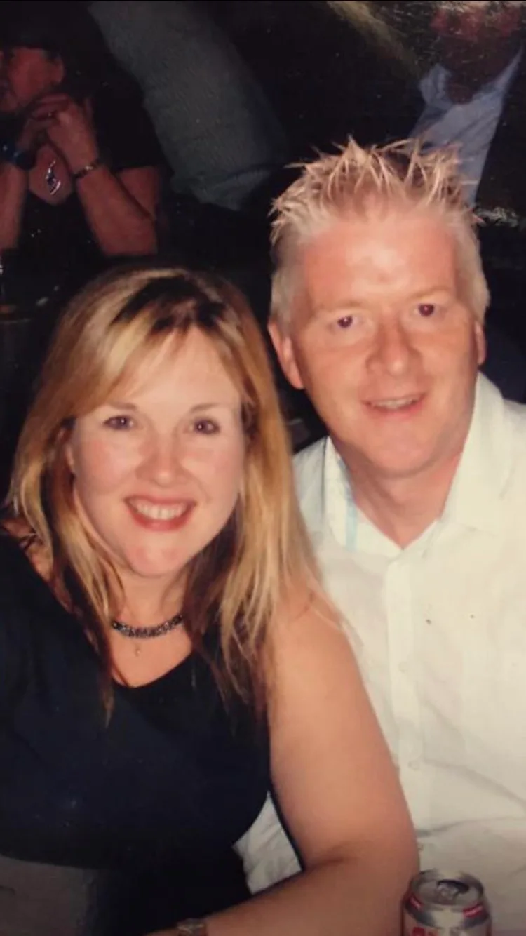 A couple at a party, arms round each other.