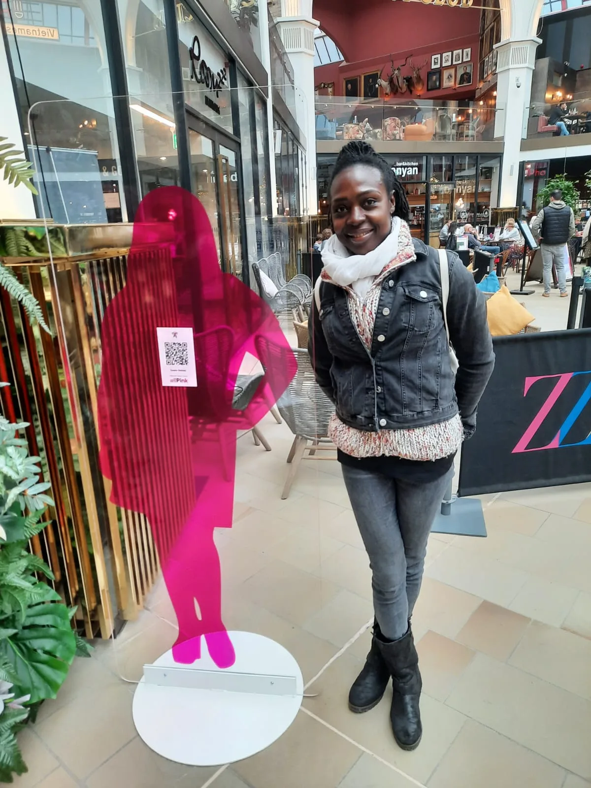 Leila Asoko beside the bright pink mannequins of a Darker Side of Pink display in a shopping centre.