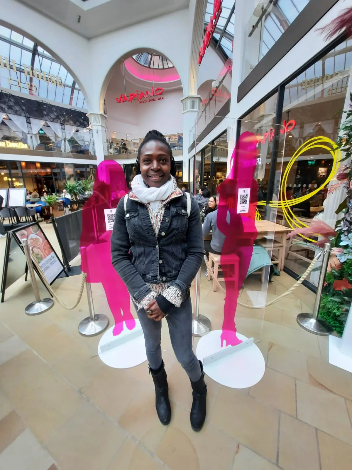 Leila Asoko standing between two bright pink mannequins in a shopping arcade.