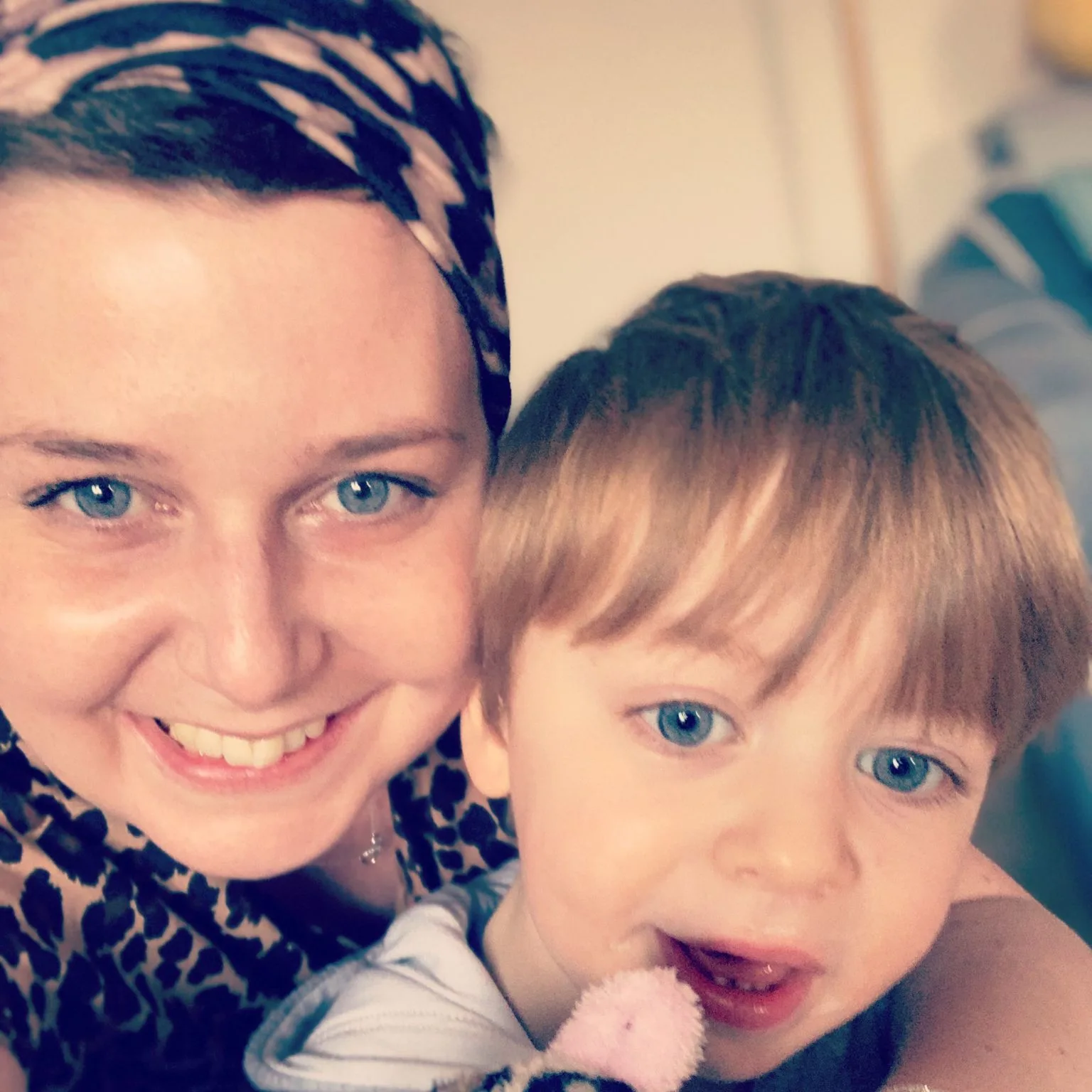 A woman in a patterned headscarf, cheek to cheek with her small son.