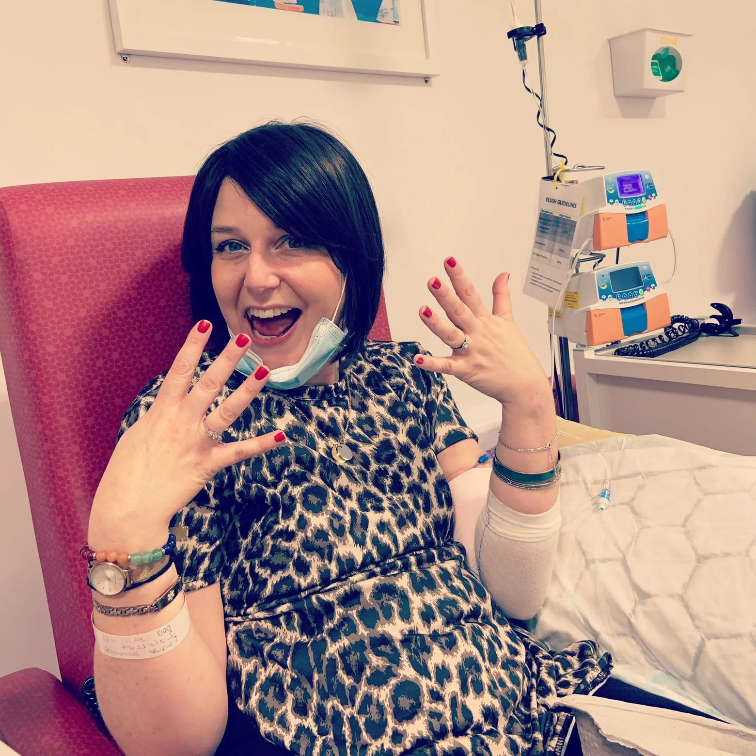 Emma in a hospital treatment chair, hands up and laughing for the camera.