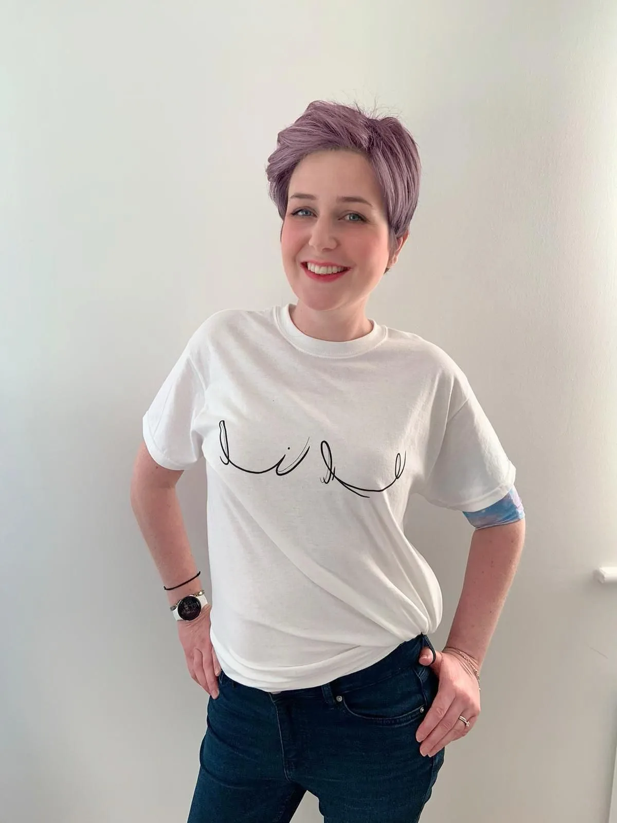 A woman in a white T-shirt printed with a line drawing, standing against a plain wall.