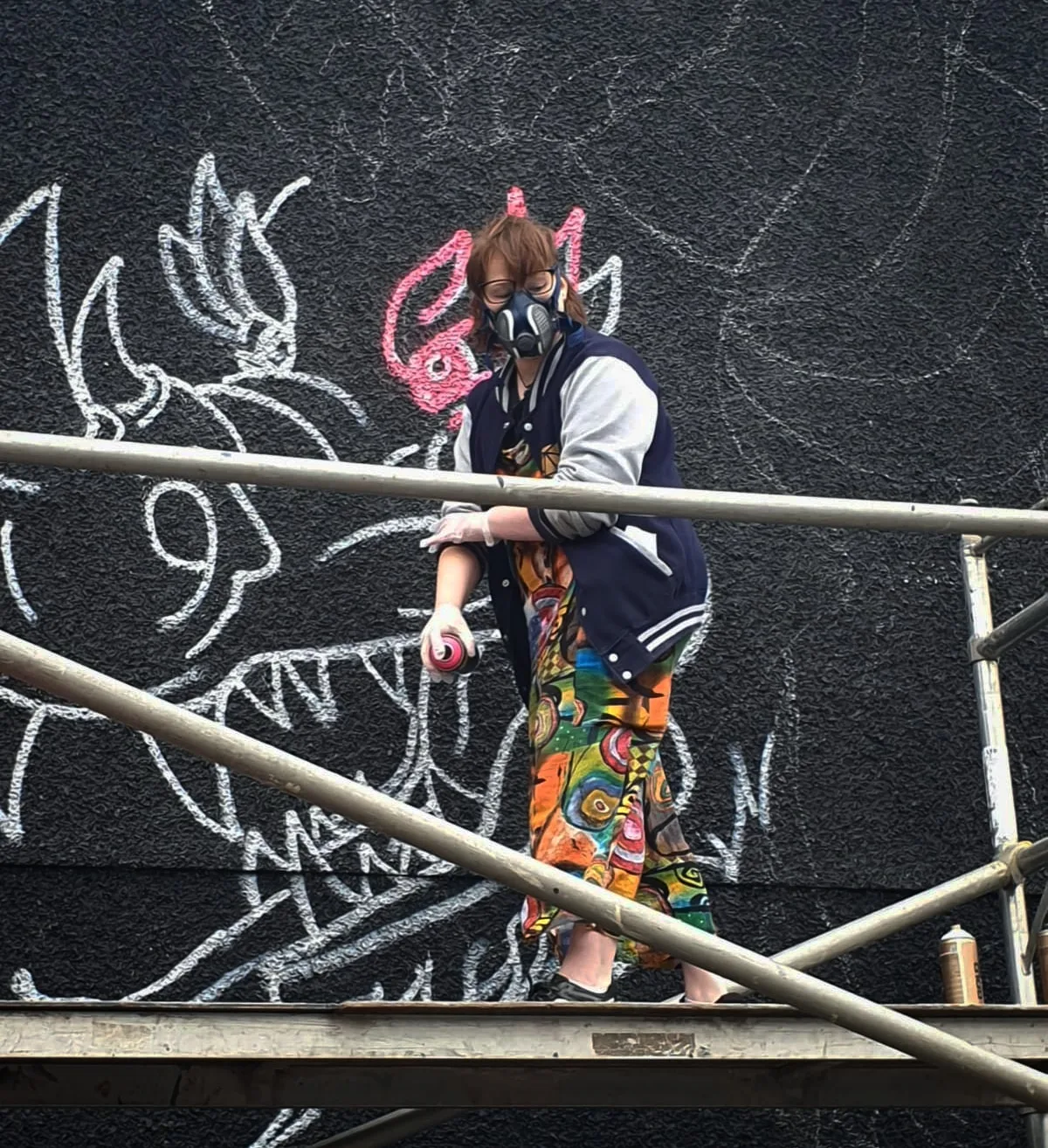Tassia Haines in a respirator, up on the scaffolding, part way through chalking out the dragon.
