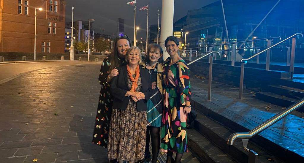 Four campaigners arm in arm on a seafront promenade at dusk.