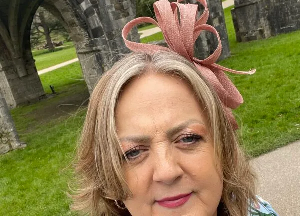 Sue Thomas in a pink fascinator, outside a ruined abbey.
